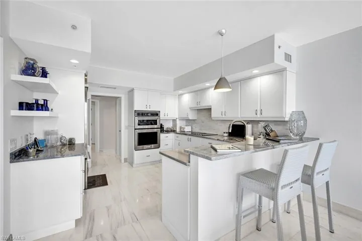 Kitchen featuring stainless steel double oven, a peninsula, backsplash, open shelves, and a kitchen breakfast bar