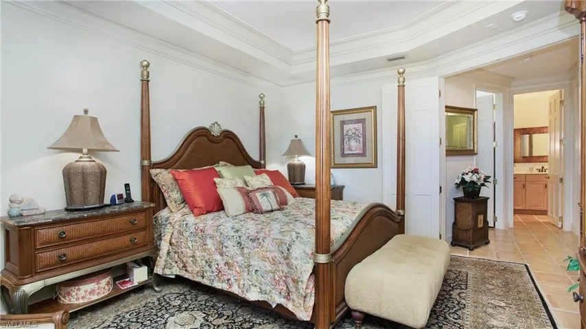 Bedroom featuring ornamental molding, connected bathroom, light tile patterned flooring, and a tray ceiling