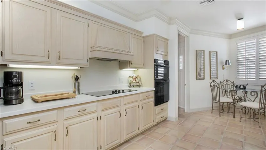 Kitchen featuring light tile patterned flooring, crown molding, black appliances, custom range hood, and cream cabinetry