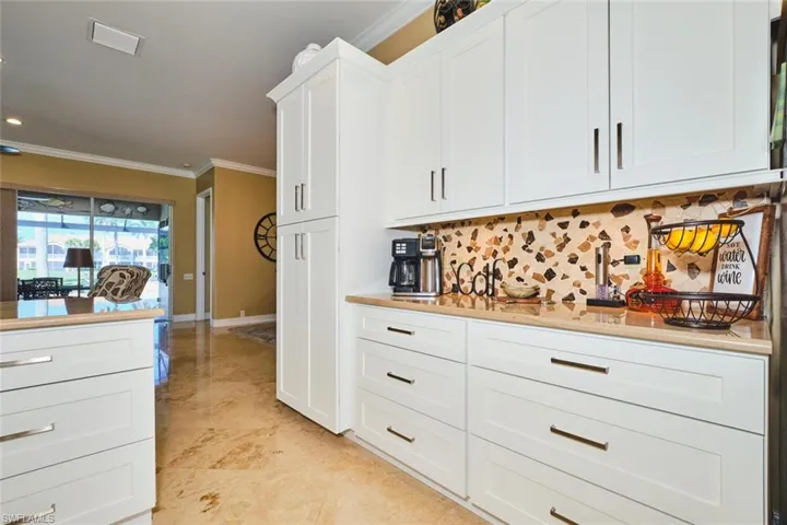 Kitchen with ornamental molding, white cabinets, tasteful backsplash, and light stone countertops