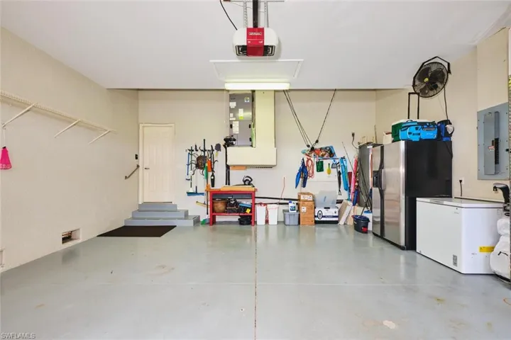 Garage featuring stainless steel fridge with ice dispenser, electric panel, and a garage door opener