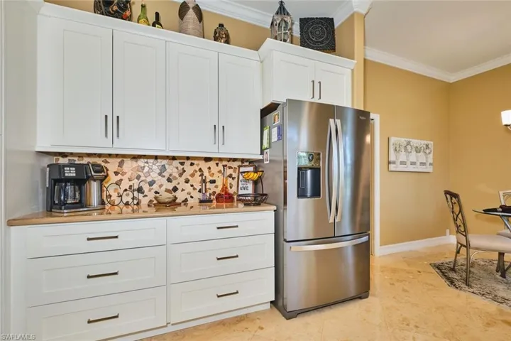 Kitchen with white cabinets, stainless steel refrigerator with ice dispenser, crown molding, backsplash, and light stone countertops