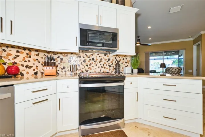 Kitchen featuring stainless steel appliances, decorative backsplash, white cabinets, crown molding, and recessed lighting