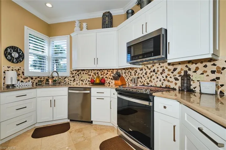 Kitchen featuring appliances with stainless steel finishes, tasteful backsplash, white cabinetry, crown molding, and light stone counters