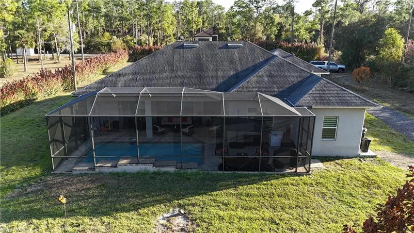 Rear view of house with a shingled roof, an outdoor pool, a yard, and a lanai