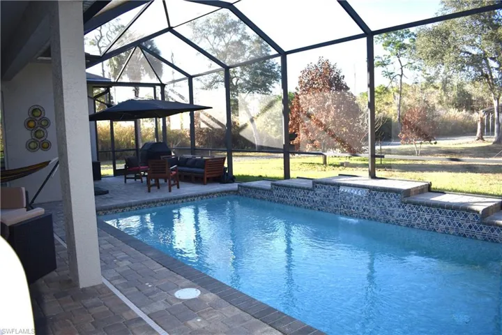 Outdoor pool featuring glass enclosure, outdoor lounge area, a sunroom, and a patio