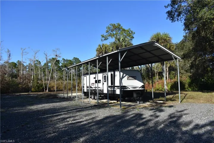 View of parking with a carport, gravel driveway, and view of wooded area