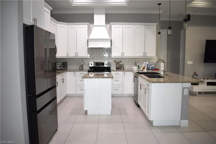 Kitchen featuring a peninsula, stainless steel appliances, light stone counters, white cabinets, and decorative light fixtures