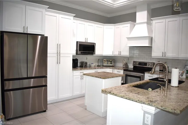 Kitchen with stainless steel appliances, white cabinetry, light stone counters, a peninsula, and crown molding