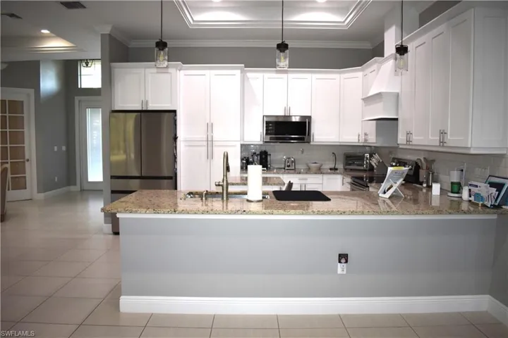 Kitchen with a raised ceiling, stainless steel appliances, white cabinets, a peninsula, and decorative light fixtures