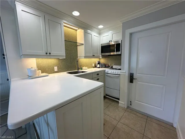 Kitchen with sink, kitchen peninsula, white range oven, crown molding, and white cabinets