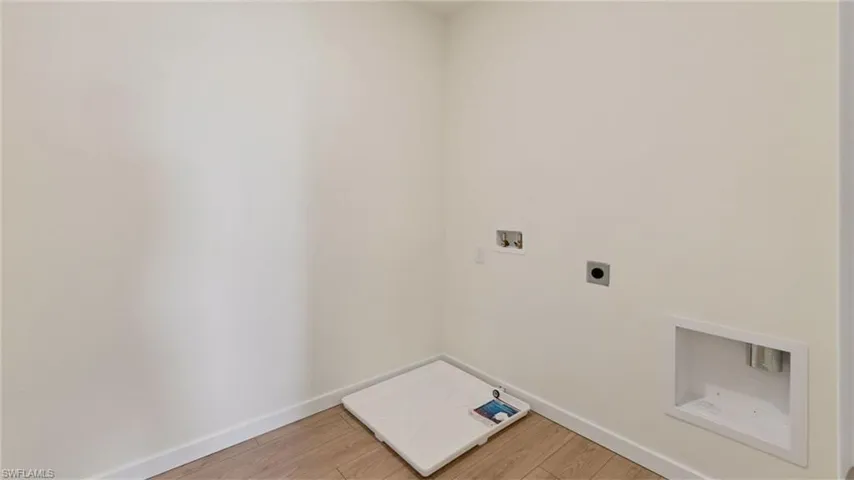 Utility space featuring wood-finish flooring, a recessed dryer vent, and a dedicated floor drain pan