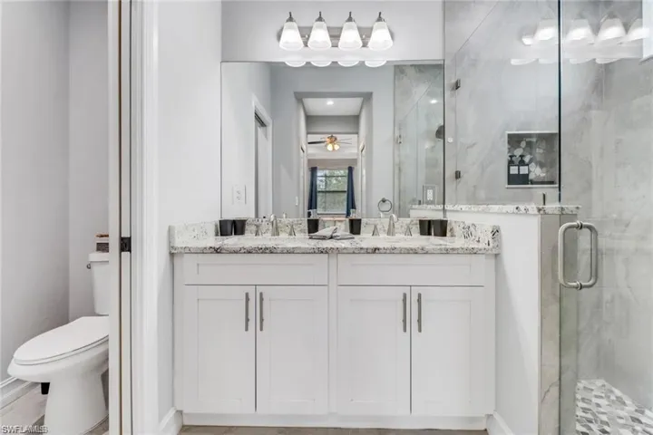 Full bath featuring a marble finish shower, double vanity, and a ceiling fan