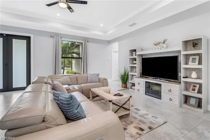 Living room with ceiling fan, a raised ceiling, recessed lighting, and french doors