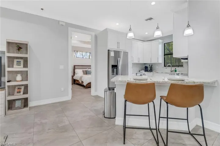 Kitchen featuring light stone countertops, white cabinets, stainless steel refrigerator with ice dispenser, a peninsula, and a kitchen bar