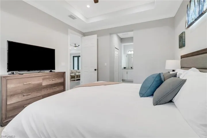 Bedroom with crown molding, ensuite bath, a ceiling fan, and a tray ceiling