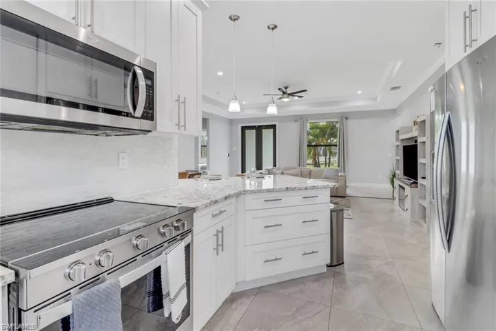 Kitchen with stainless steel appliances, light stone countertops, white cabinetry, ceiling fan, and a tray ceiling
