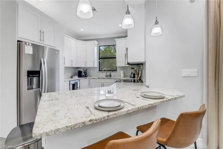 Kitchen with a breakfast bar, a peninsula, stainless steel refrigerator with ice dispenser, light stone counters, and white cabinetry