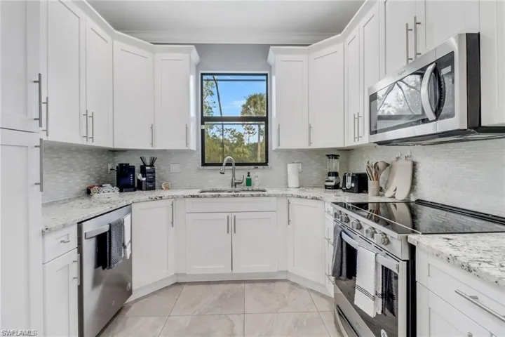 Kitchen with stainless steel appliances, white cabinetry, light stone counters, and backsplash