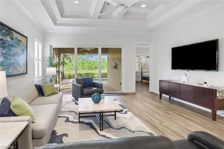 Living area featuring light wood-style floors, crown molding, a ceiling fan, coffered ceiling, and beam ceiling