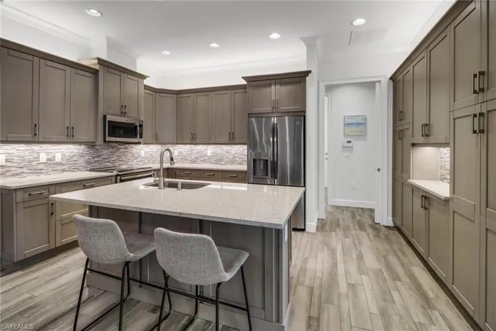 Kitchen featuring light wood-type flooring, sink, an island with sink, appliances with stainless steel finishes, and ornamental molding