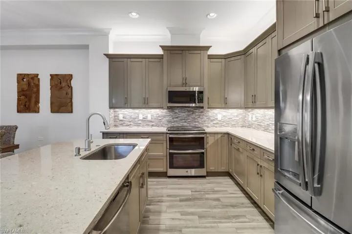 Kitchen with light stone counters, ornamental molding, sink, light hardwood / wood-style flooring, and stainless steel appliances
