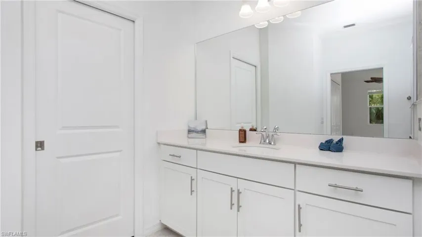 Full vanity with a white countertop and integrated sink, white cabinetry with silver hardware, large wall-mounted mirror, and overhead vanity lighting
