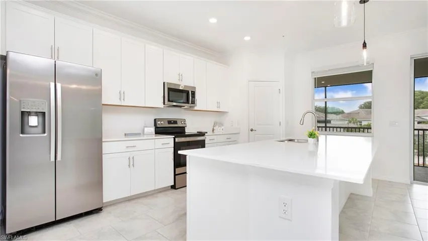 Modern kitchen featuring white cabinetry, stainless steel appliances, a center island with a sink, light-toned flooring, and a large window