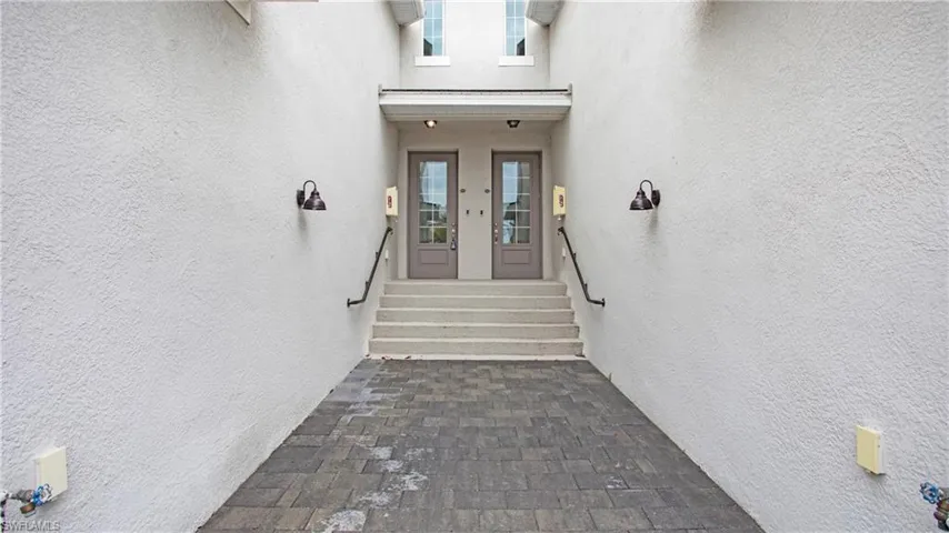 Paver walkway leading to a stucco exterior with dual entry doors