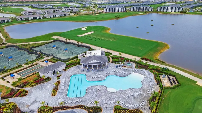 Expansive community recreation area featuring a large, multi-section swimming pool, a separate spa, multiple tennis courts, bocce ball courts, and manicured green spaces