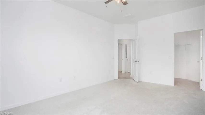 Spacious room featuring light-colored carpeting, white baseboards, and a ceiling fan