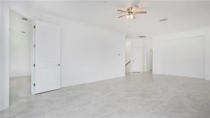 Spacious interior with neutral wall tones, large format tile flooring, crown molding, and a ceiling fan with integrated lighting