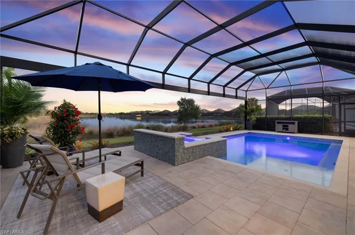 Pool at dusk with glass enclosure, a water view, a patio, and a hot tub