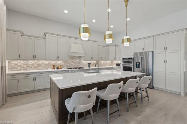 Kitchen with sink, stainless steel appliances, a kitchen breakfast bar, pendant lighting, and custom range hood
