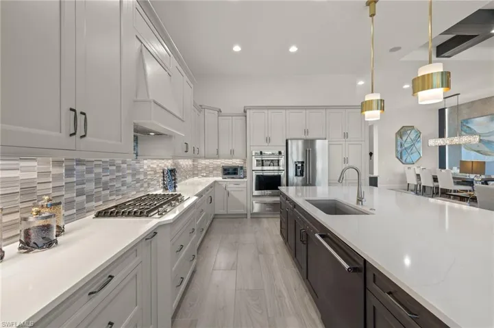 Kitchen featuring custom exhaust hood, sink, hanging light fixtures, light stone countertops, and stainless steel appliances