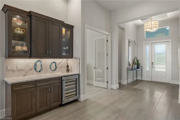 Bar featuring hanging light fixtures, light wood-type flooring, dark brown cabinets, light stone counters, and beverage cooler