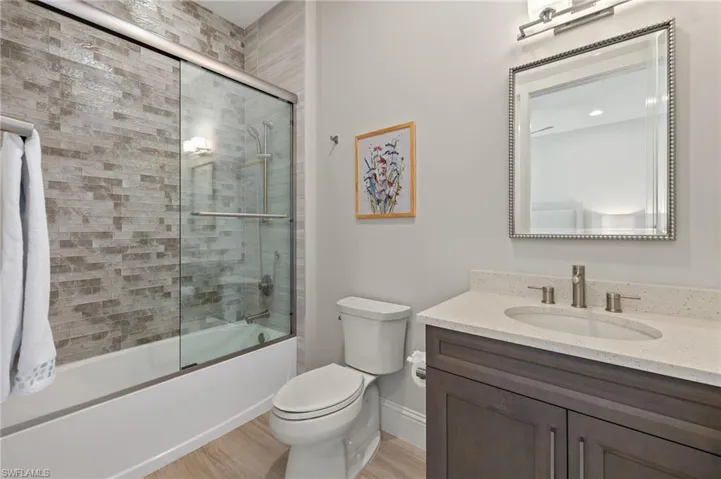 Full bathroom with bath / shower combo with glass door, vanity, wood-type flooring, and toilet