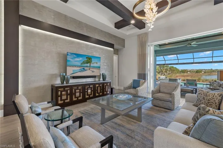 Living room with ceiling fan with notable chandelier, beam ceiling, and wood-type flooring