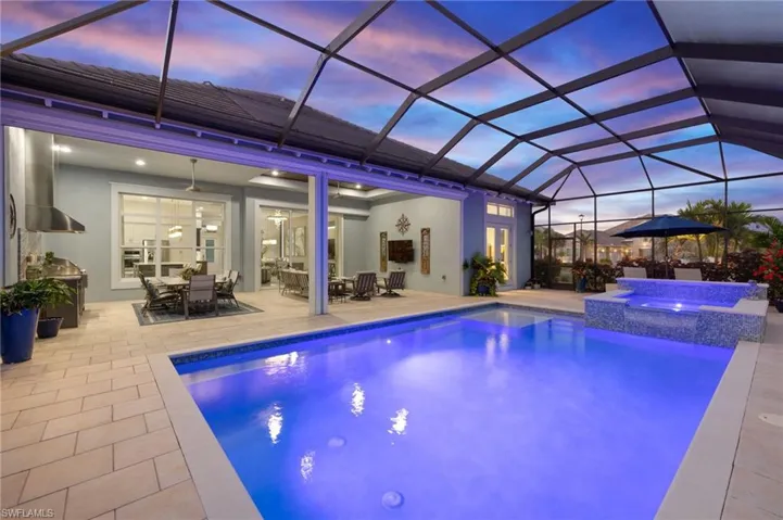 Pool at dusk with glass enclosure, ceiling fan, an in ground hot tub, and a patio