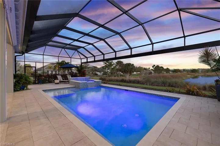 Pool at dusk featuring glass enclosure, a patio area, and an in ground hot tub