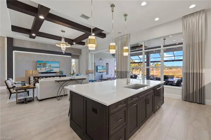 Kitchen with coffered ceiling, sink, hanging light fixtures, an island with sink, and beamed ceiling