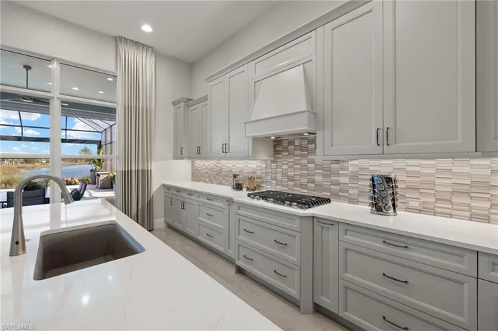 Kitchen with decorative backsplash, premium range hood, sink, gray cabinets, and stainless steel gas stovetop