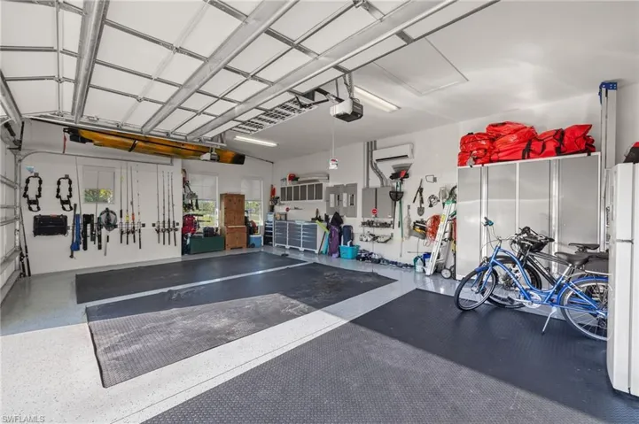 Garage with a wall mounted air conditioner, white refrigerator, and a garage door opener