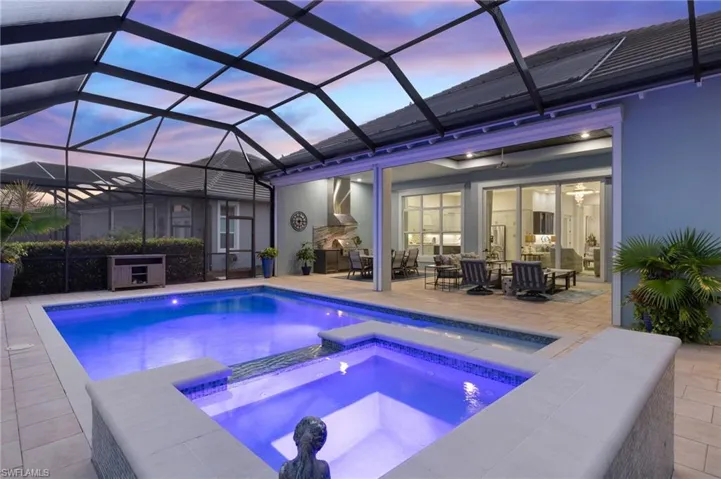 Pool at dusk with an outdoor living space with a fireplace, ceiling fan, a lanai, an in ground hot tub, and a patio area
