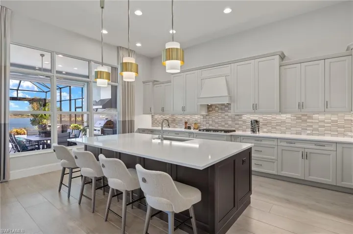 Kitchen with premium range hood, a kitchen island with sink, sink, decorative light fixtures, and light hardwood / wood-style flooring