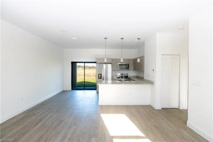 Open-concept living space featuring wood-finish flooring, recessed lighting, and a kitchen with stainless steel appliances, stone countertops, and wood-finish cabinetry