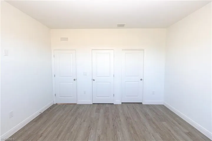 Wood-finish flooring with white baseboards, three white panel doors, and neutral wall tones