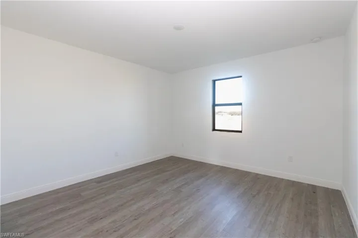 Recessed ceiling lighting, wood-finish flooring, white wall finishes, and a single window with a dark frame