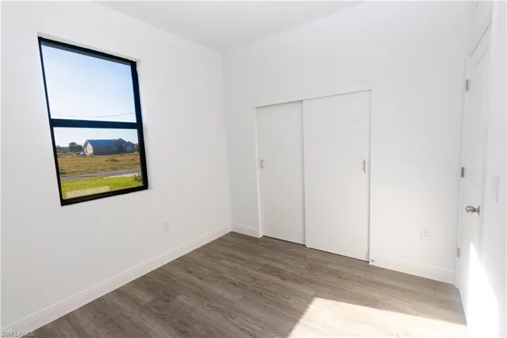 Neutral white walls, wood-finish flooring, black-framed window, and sliding closet doors