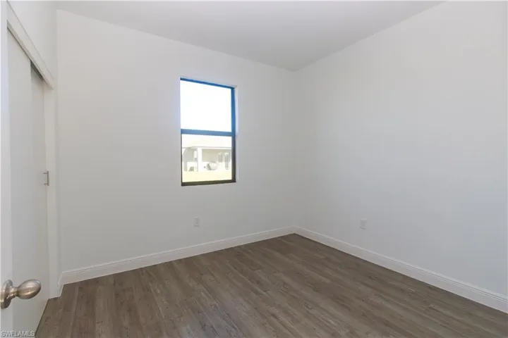 Wood-finish flooring, white painted walls, and a single window with dark framing